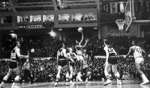 A group of men playing basketball in front of an audience.