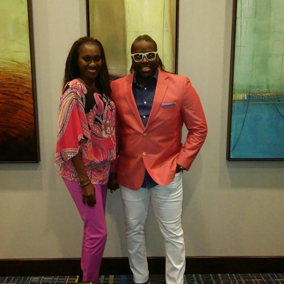 A man and woman posing for the camera in front of paintings.