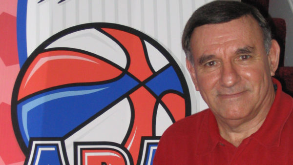 A man in red shirt standing next to a basketball sign.