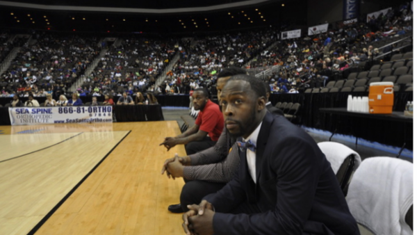 Three men sitting on a basketball court.